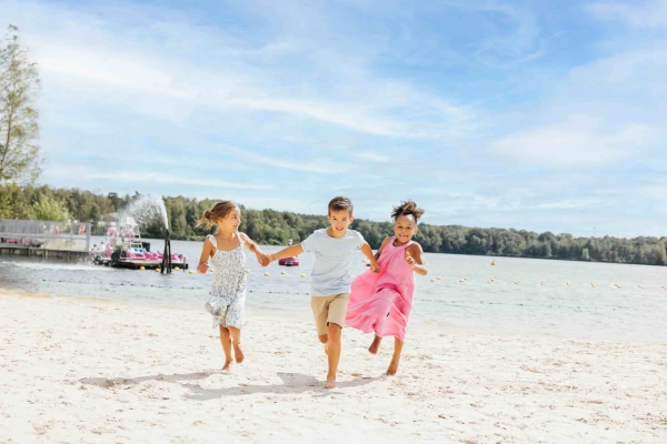 Drie lachende kinderen rennen hand in hand over het zandstrand van Lake Resort Beekse Bergen