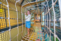 Meisje klimt lachend door een lange, avontuurlijke touwtunnel in het indoor speelparadijs van Landal Orveltermarke.