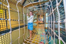 Meisje klimt lachend door een lange, avontuurlijke touwtunnel in het indoor speelparadijs van Landal Orveltermarke.