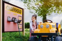  Lachend meisje speelt met een grote gele safari jeep bij een onderhoud bord in de speeltuin van Safari Resort Beekse Bergen