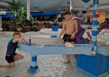 Kinderen spelen in het kinderbad met stroomversnelling en sproeiers bij Recreatiepark De Leistert