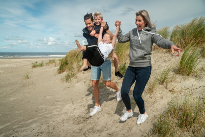 Een vrolijk gezin met twee kinderen rent lachend hand in hand van een duin af op het eiland Schiermonnikoog.