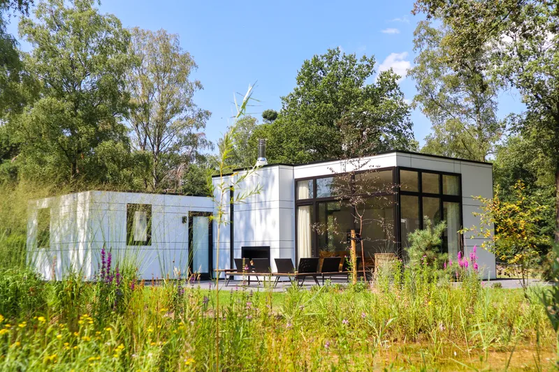 Een moderne, witte design vakantiewoning met een terras, omgeven door wilde bloemen en het groen van de Veluwe op Droompark Hooge Veluwe.
