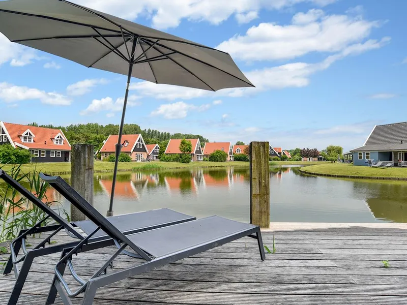 Een zonnige houten vlonder met twee ligbedden en een parasol direct aan het water, met uitzicht op de vakantiehuizen van Landal Waterparc Veluwemeer