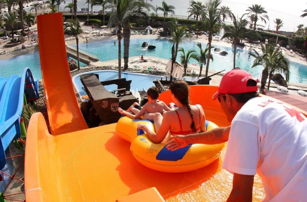 Kinderen glijden van oranje boomerang glijbaan in waterpark op Gran Canaria