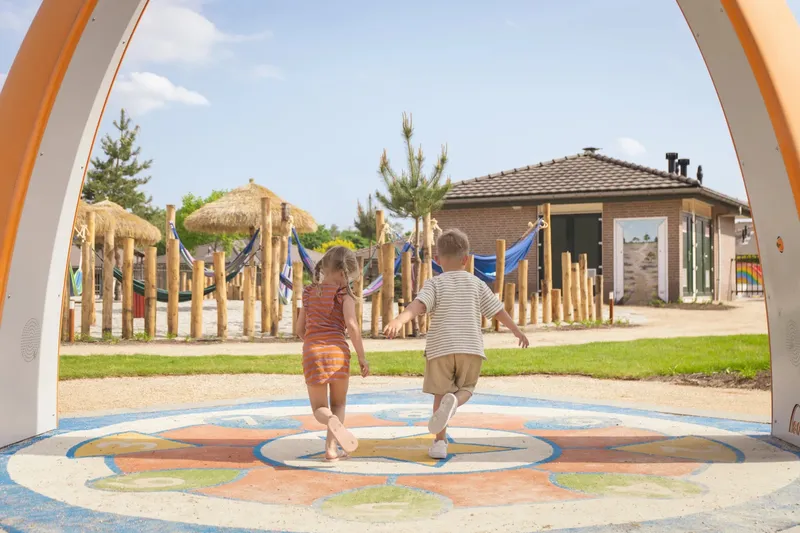 Twee jonge kinderen rennen en spelen op de kleurrijke, interactieve speelvloer van de Sona speelboog in de Speelvallei op Recreatiepark de Boshoek.