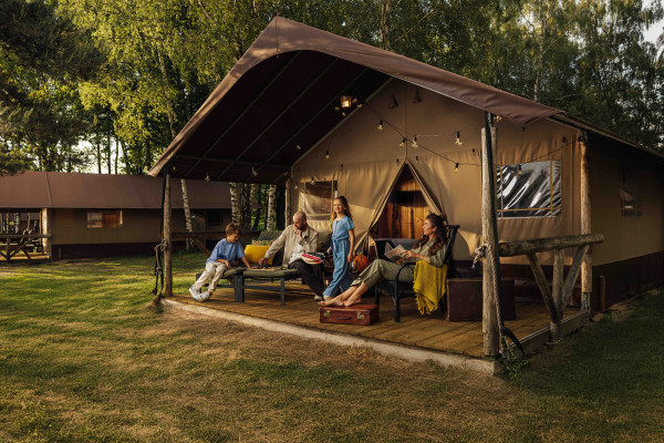Gezin van vier ontspant samen op de veranda van een ruime safaritent in het bos van Lake Resort Beekse Bergen