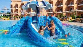 Een vader en dochter hebben plezier op een kleine blauwe kinderglijbaan in het zwembad van Three Corners Sunny Beach Resort.