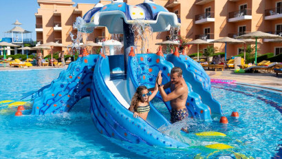 Een vader en dochter hebben plezier op een kleine blauwe kinderglijbaan in het zwembad van Three Corners Sunny Beach Resort.