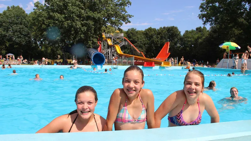 Drie lachende meisjes in bikini poseren in het grote buitenzwembad van Waterspeelpark Splesj bij Molecaten Park Bosbad Hoeven.