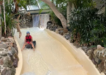Kind glijd van wildwaterbaan bij  subtropisch zwembad Aqua Mundo van Center Parcs Heijderbos