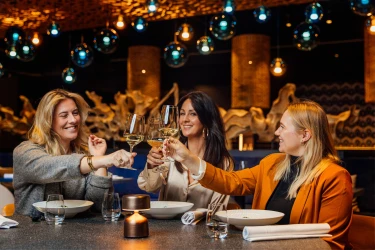 Drie vrouwen proosten met witte wijn tijdens een diner in restaurant Moto van Safari Hotel Beekse Bergen