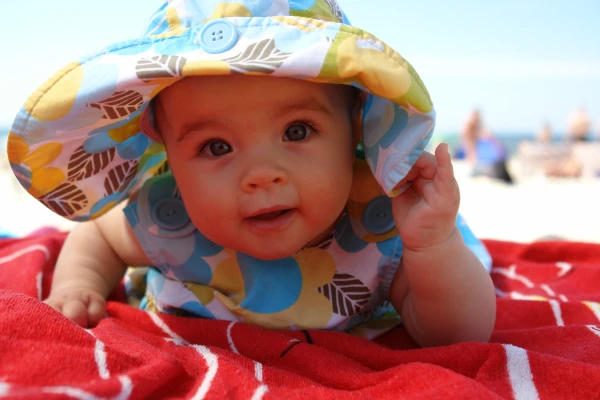 Baby ligt op zijn buik op het strand met een hoedje op