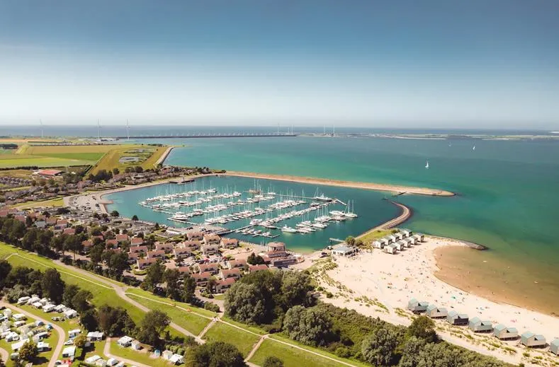 Luchtfoto van Roompot Beach Resort in Zeeland, met uitzicht over de jachthaven, het strand met strandhuisjes en de Oosterscheldekering.