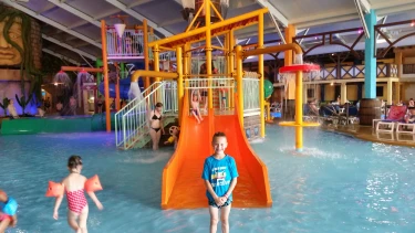 Kind staat voor grote oranje glijbaan bij een waterspeeltuin van Slagharen. 