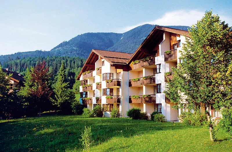 De buitenkant van het Dorint Sporthotel in Garmisch-Partenkirchen, omgeven door groene gazons en met de Beierse Alpen op de achtergrond.
