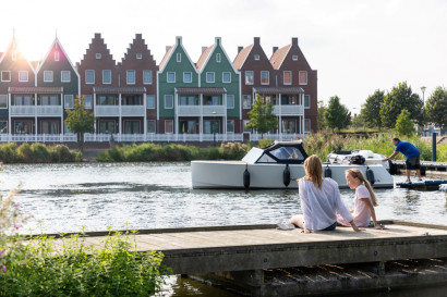 Een moeder en dochter genieten van het uitzicht over het water, zittend op een steiger met de typische Volendamse vakantiehuizen op de achtergrond.