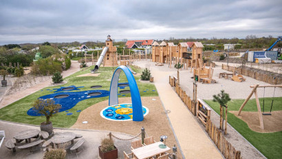 Overzicht van de grote buitenspeeltuin van zand en hout met klimtoestellen en trampolines bij Strandpark De Zeeuwse Kust.