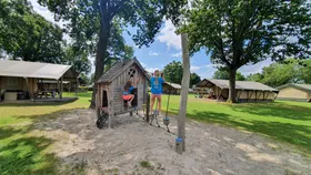 Kinderen spelen in houten speeltuin op camping veld met safaritenten