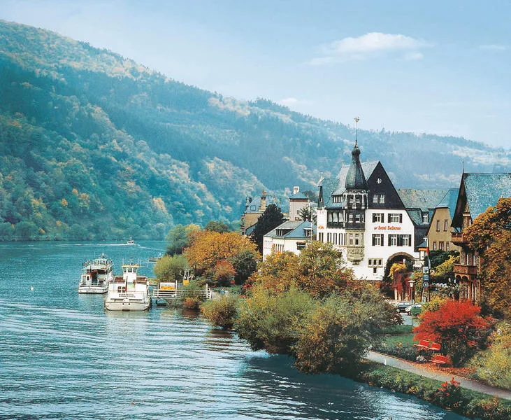 Sfeervol zicht op Romantik Jugendstilhotel Bellevue aan de Moezel in de herfst, met rondvaartboten aan de kade en heuvels met herfstkleuren.