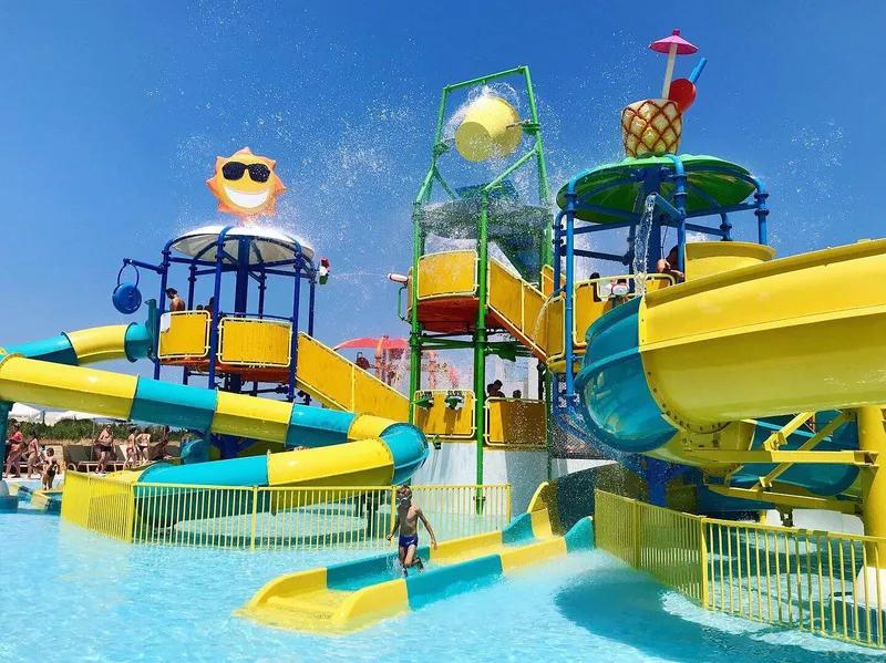 Kleurrijk waterspuitpark voor kinderen met kleine glijbanen, een ananas-fontein en een lachende zon-decoratie in het waterpark.