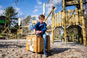 Jongen speelt in de avontuurlijke buitenspeeltuin met houten klimtoestellen en zand op het kindvriendelijke vakantiepark Landal De Lommerbergen.