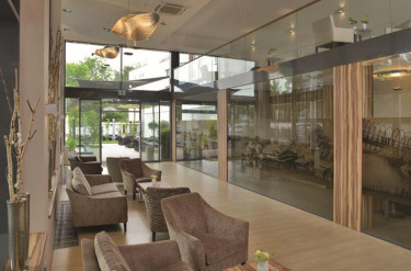 De ruime lobby en lounge van Parkhotel Oberhausen met glazen wanden en uitzicht op het terras