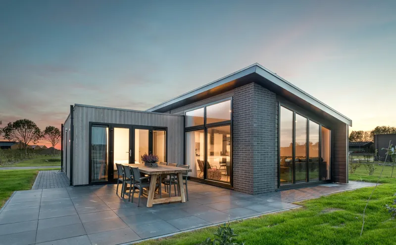 Een luxe, moderne dijklodge op Vakantiepark Zeedijk bij zonsondergang, met een verlicht interieur en een ruim terras in de polder van Zuid-Holland.
