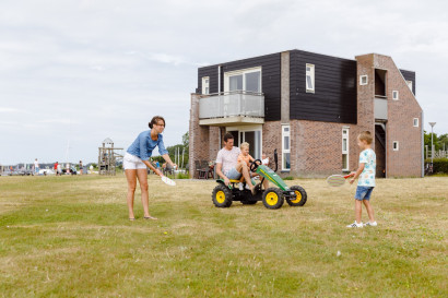 Een gezin vermaakt zich op het grasveld bij hun vakantiehuis op RCN de Schotsman in Zeeland, met een skelter en een potje badminton.