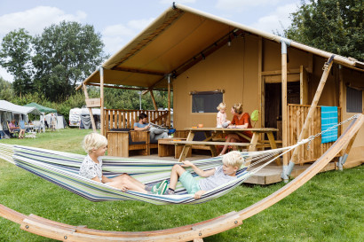 Twee jongens ontspannen in een hangmat voor hun luxe glamping safaritent op een vakantiepark in Zeewolde.