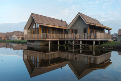 Een luxe, vrijstaande waterwoning op palen met een houten veranda, die prachtig reflecteert in het kalme water van de Reeuwijkse Plassen bij Landal.