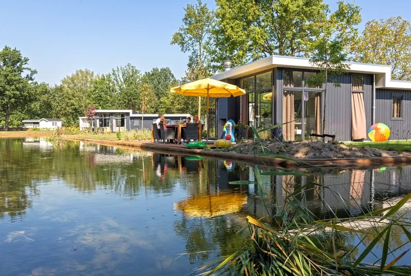 Moderne vakantiewoning met een vlonderterras en gele parasol, direct gelegen aan het water op EuroParcs Resort Limburg.