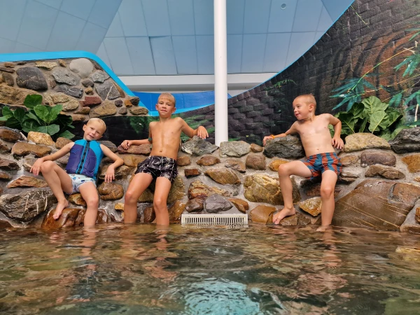 Kinderen staan tegen rotswand aan in het zwembad