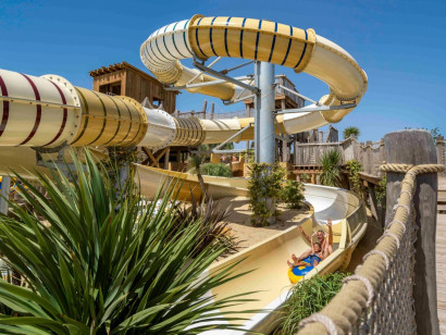 Kind glijdt met een opblaasband van de grote, kronkelende waterglijbaan in het aquapark van Camping Le Sérignan Plage.
