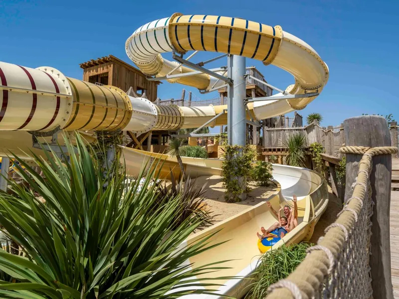Kind glijdt met een opblaasband van de grote, kronkelende waterglijbaan in het aquapark van Camping Le Sérignan Plage.