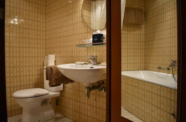 De retro badkamer van Hotel Atlanta in Limburg met beige tegels een toilet een wastafel en een bad
