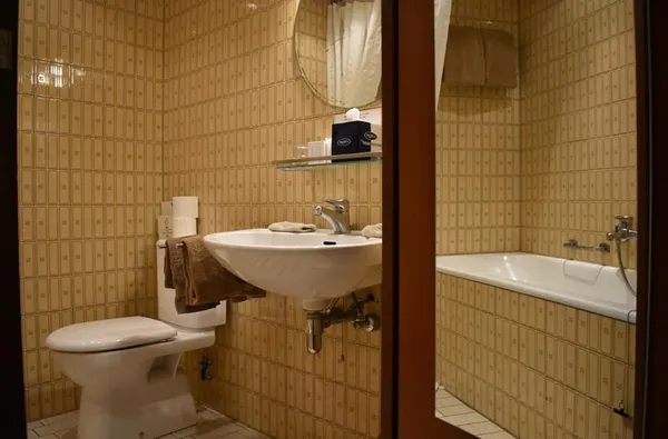 De retro badkamer van Hotel Atlanta in Limburg met beige tegels een toilet een wastafel en een bad