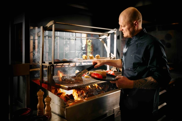 Chef‑kok bereidt gegrilde groenten en vlees op grote open houtskoolgrill tijdens live cooking diner in restaurant van Safari Resort Beekse Bergen