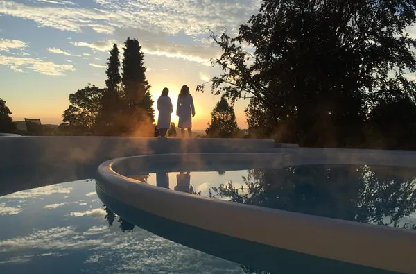 Gasten in badjas genieten van de zonsondergang bij het wellness buitenzwembad van Hotel Atlanta in het Limburgse heuvellandschap