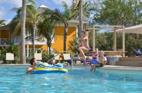 Kinderen die met een bommetje in het zwembad van CHOGOGO Resort op Curaçao springen, omringd door palmbomen.