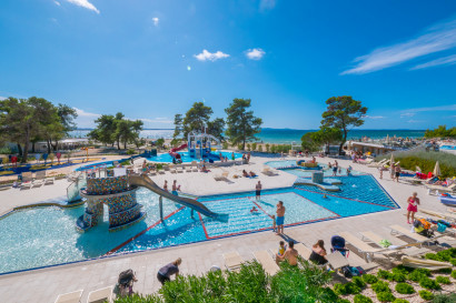 Overzicht van het kindvriendelijke zwembadcomplex van Zaton Holiday Resort met een glijbaan, spelende kinderen, en uitzicht op het strand en de zee in Kroatië.