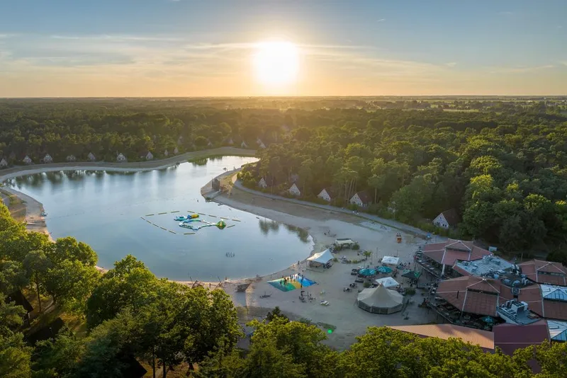 Luchtfoto van Landal 't Loo op de Veluwe met de grote recreatieplas, het strand en de omliggende bossen tijdens zonsondergang.