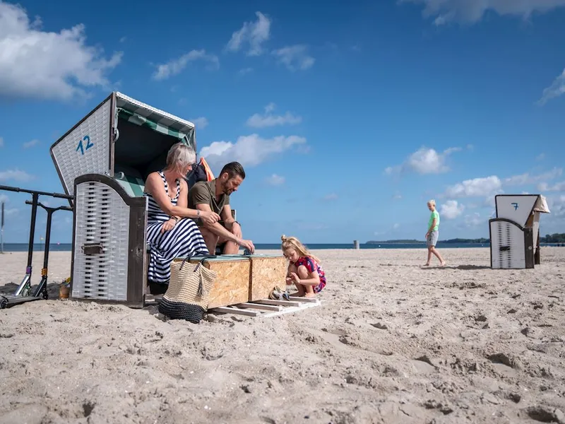 Een gezin met een jong dochtertje geniet van een zonnige dag op het strand bij Landal Travemünde, zittend in een typische Duitse strandkorf.