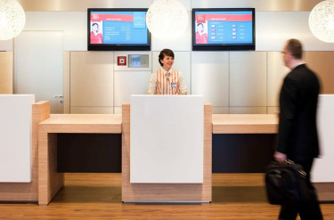 De receptie van Ibis Hotel Aken met een receptioniste die een gast verwelkomt