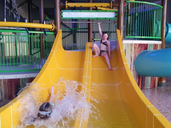 Kinderen glijden van dubbele glijbanen op een vakantiepark met subtropisch zwembad. 