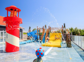 Kinderen spelen in de waterspeeltuin met een grote vuurtoren en glijbaan op Strandpark De Zeeuwse Kust in Zeeland.