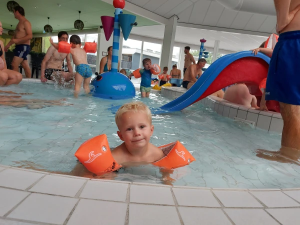 Kind drijft met zwembandjes om in het kinderzwemnbad vol waterattracties. 